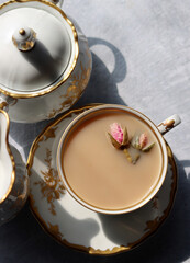 Cup of tea with milk and roses. Tea in beautiful vintage cup. Close up photo of hot aromatic beverage. 
