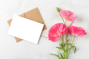 Blank greeting card and pink poppy flowers bouquet on white background. flat lay. mock up. top view