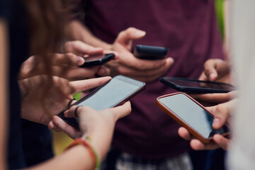 Lets see what our other friends are doing. Closeup of a group of young unrecognizable people standing in a circle while browsing on their mobile phones outside during the day.