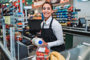 Beautiful young female cashier working at a grocery store. - obrazy, fototapety, plakaty