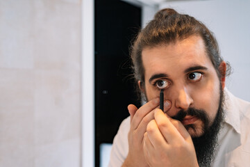 Young man applying eye make-up in the bathroom. Using eyeliner pencil - obrazy, fototapety, plakaty