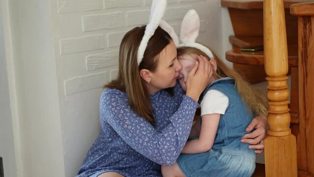 a mother soothes her crying daughter on the wooden stairs of the house. 
