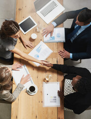 Lets work together to win together. High angle shot of a group of businesspeople shaking hands during a meeting in an office.