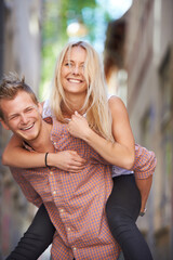 Obraz premium Having fun in the streets. A young man giving his beautiful girlfriend a piggyback ride in the street.