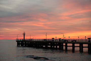 Fishing pier on the ocean with a colorful and golden sunset. Ocean beach sunrise and dramatic colorful sky clouds.