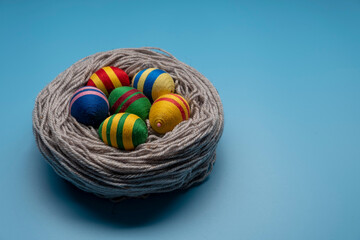 Handcrafted Easter decorations from thread. Multicolor eggs made from yarn and thread on blue background.