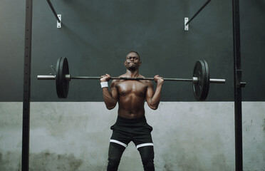 Fototapeta na wymiar Sweat a lot, gain a lot. Shot of a muscular young man doing an overhead press with a barbell in a gym.