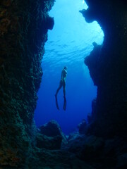 woman lady free diving apnea underwater in a cave cave with nice blue ocean scenery