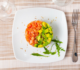 Delicious seafood tartare made of raw salmon, onion and avocado served with arugula and capers
