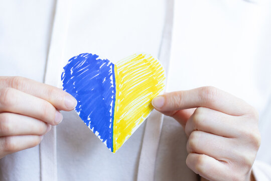 Female hands holding heart painted in Ukrainian flag colors. A close-up. The concept of love, peace, justice, freedom for Ukraine. Stop war and violence in Ukraine.