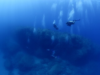 scuba divers around a reef underwater deep blue water big rocks  air bubbles rising
