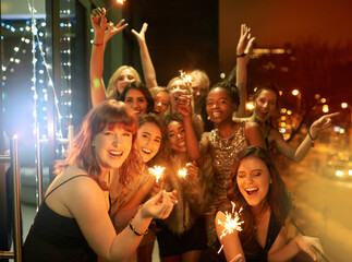 Sparkling into the New Year. Shot of a group of girlfriends having fun with sparklers on a balcony...