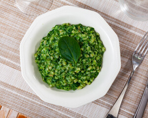 Portion of boiled pearl barley with spinach served on table.