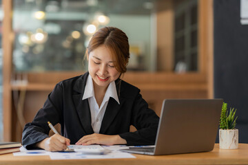 Beautiful Asian business woman sitting on her workplace in the office. Young woman working for financial document data charts with laptop in the office