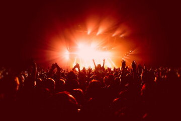 Fototapeta na wymiar A crowded concert hall with scene stage in red lights, rock show performance, with people silhouette, colourful confetti explosion fired on dance floor air during a concert festival
