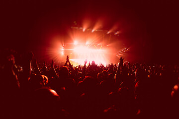 Fototapeta na wymiar A crowded concert hall with scene stage in red lights, rock show performance, with people silhouette, colourful confetti explosion fired on dance floor air during a concert festival