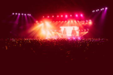 A crowded concert hall with scene stage in red lights, rock show performance, with people...