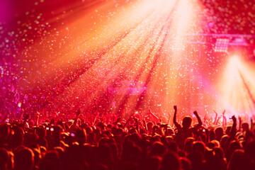 A crowded concert hall with scene stage in red lights, rock show performance, with people...