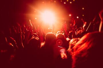 A crowded concert hall with scene stage in red lights, rock show performance, with people...