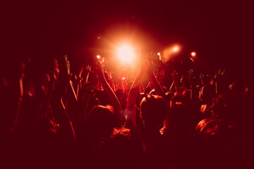 Plakat A crowded concert hall with scene stage in red lights, rock show performance, with people silhouette, colourful confetti explosion fired on dance floor air during a concert festival