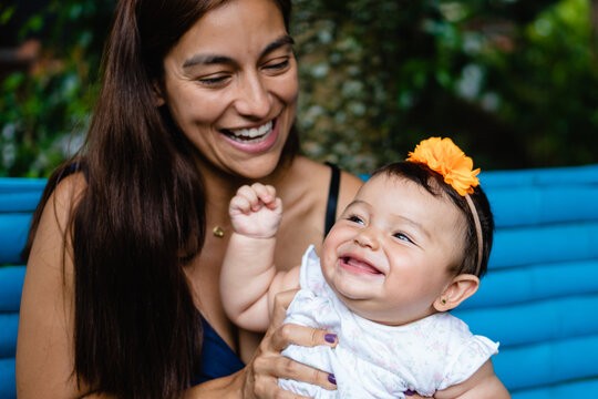 young latina mom with her smiling baby playing outdoors