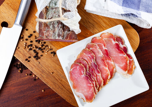 Thinly sliced cured pork sirloin meat with spices on wooden cutting board