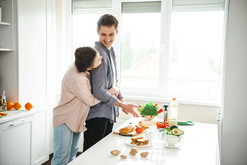 Loving woman embracing her boyfriend from behind spending time in kitchen. Vegetarian healthy food. Activity relationship. Cooking, together, kitchen