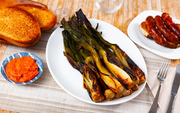 Traditional Catalan grilled calcots served with romesco sauce for dipping, pork sausage botifarra and browned toasted bread..