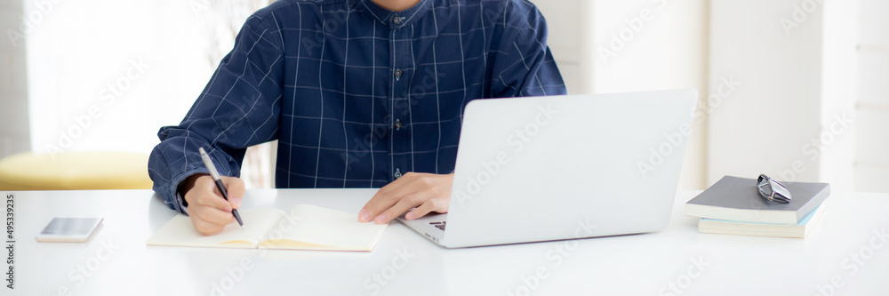 Poster young asian business man writing on notebook for planning working and using laptop computer on desk 