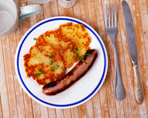 Potato pancakes with grilled sausage served on plate on wooden table.