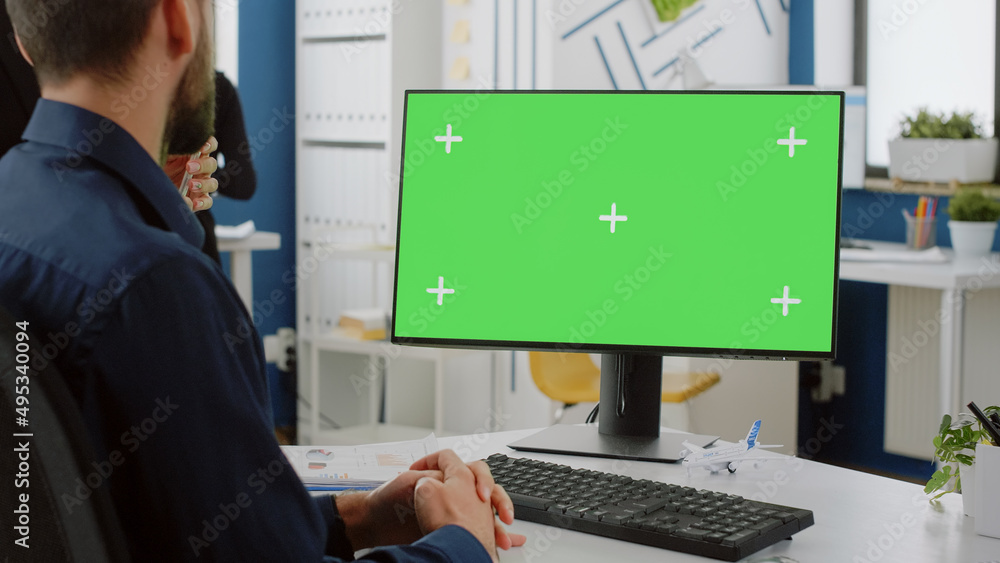Poster close up of computer with horizontal green screen on desk and colleagues talking about business stra