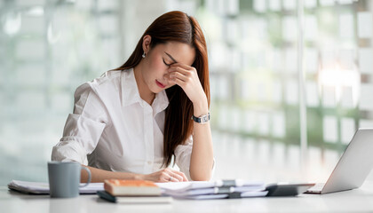 Young Asian businesswoman working on laptop computer, stressed has a headache and thinks hard from work at the office. - Powered by Adobe