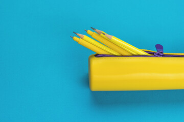 An open yellow pencil case with pens and pencils on a blue background. Flat lay.