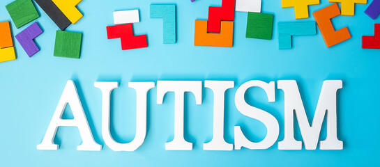 AUTISM text with colorful wood puzzle pieces, geometric shape block on blue background. Concepts of health, Autistic Spectrum disorder and world Autism awareness day