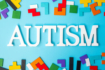 AUTISM text with colorful wood puzzle pieces, geometric shape block on blue background. Concepts of health, Autistic Spectrum disorder and world Autism awareness day