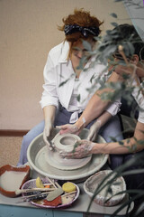 A couple in love in white shirts and jeans, a date in a pottery workshop, working together on one potter's wheel