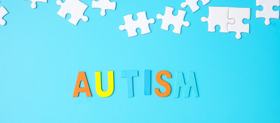 AUTISM text with white puzzle jigsaw pieces on blue background. Concepts of health, Autistic...