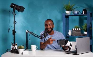 Vlogger recording podcast review for virtual reality goggles pointing out advantages talking into...