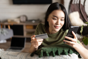 Young asian woman buying from online shop, using mobile phone and credit card, shopping from home - obrazy, fototapety, plakaty