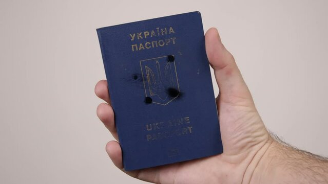 Holes in shot Ukrainian passport. Concept of occupation of the country, the war in Ukraine. Male hand holding a blue document. Russian aggression, occupiers