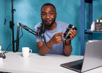 Vlogger recording podcast review for dslr zoom lens pointing out advantages talking into studio...