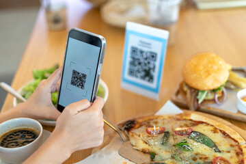 Woman's hand uses a phone to scan a qr code in a restaurant to receive a discount or pay for food. ...