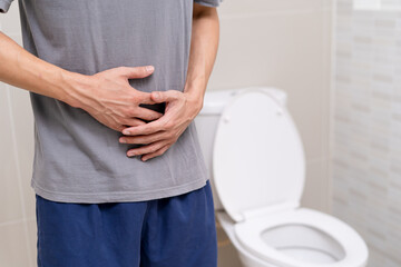man standing has diarrhea and severely toxic food. Man touch belly in the bathroom. Abdominal pain, Diarrhea, Colon cancer concept