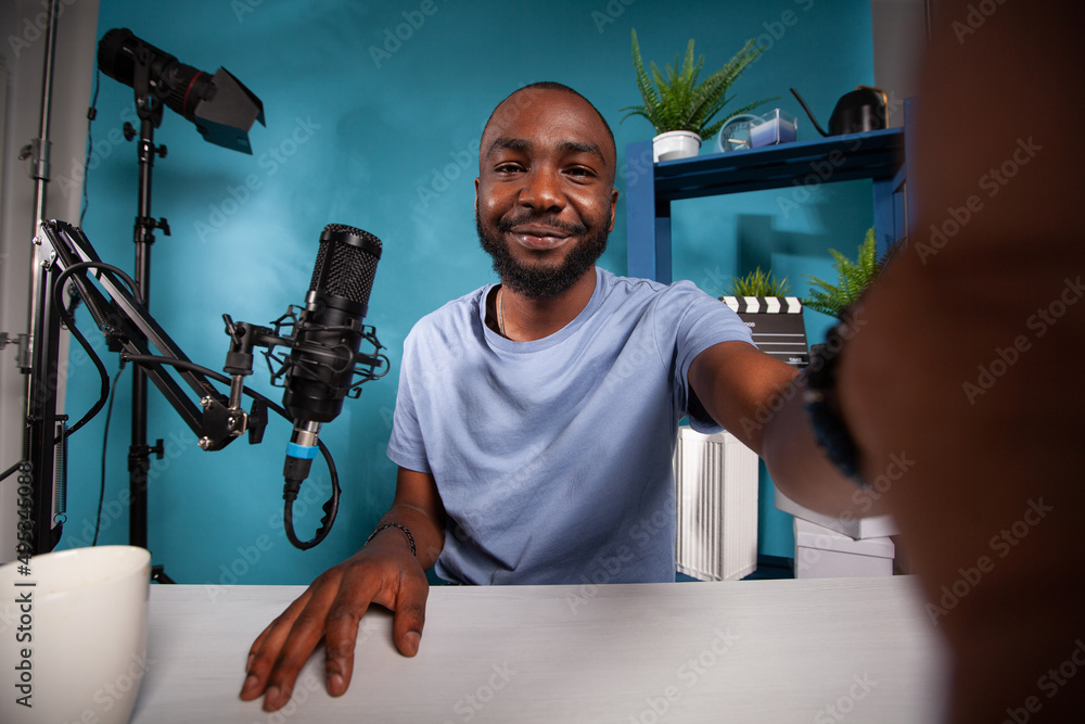Poster wide angle view of relaxed influencer taking a selfie smiling at camera in podcasting vlog studio in