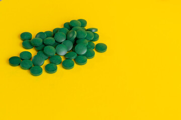 Spirulina round green pills on a yellow background. Vegan tablets copy space