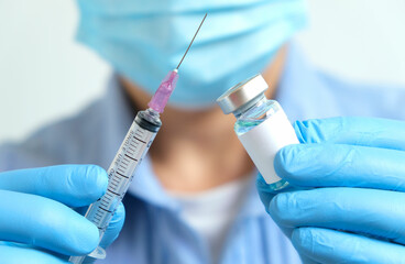doctor's hand holds a syringe and a blue vaccine bottle at the hospital. Health and medical concepts.