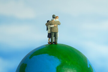 Miniature people toy figure photography. Family reunion day concept. Father hugging his wife and daughter above earth globe