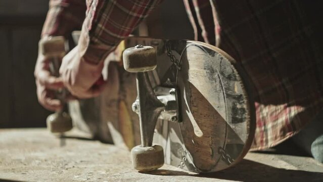 Close-up of an unrecognizable guy on a skateboard unscrewing the wheels on his board with a hex wrench. Professional skateboarding service.
