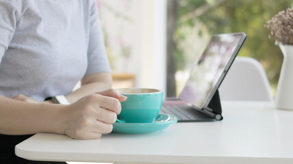 Woman's hand with a cup of coffee, sitting in the morning doing work with a laptop