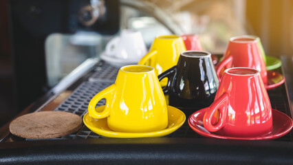 Fototapeta premium Close up to colorful ceramic upside down coffee cups on coffee machine in cafe. Multi colored upside down the coffee cups in coffee shop. Group of color tea or coffee cups. Selective Focus.